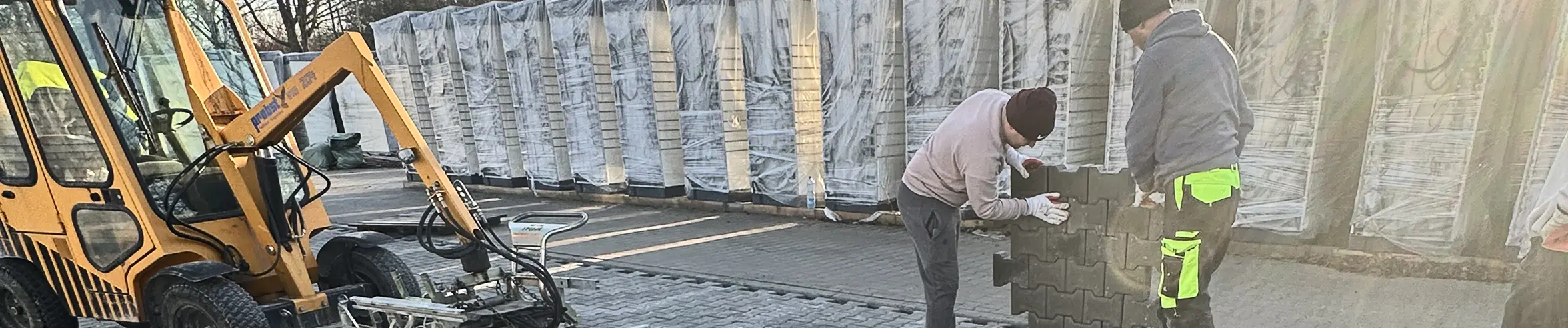 Dwóch pracowników układa płyty ażurowe na utwardzonym podłożu z pomocą minikoparki