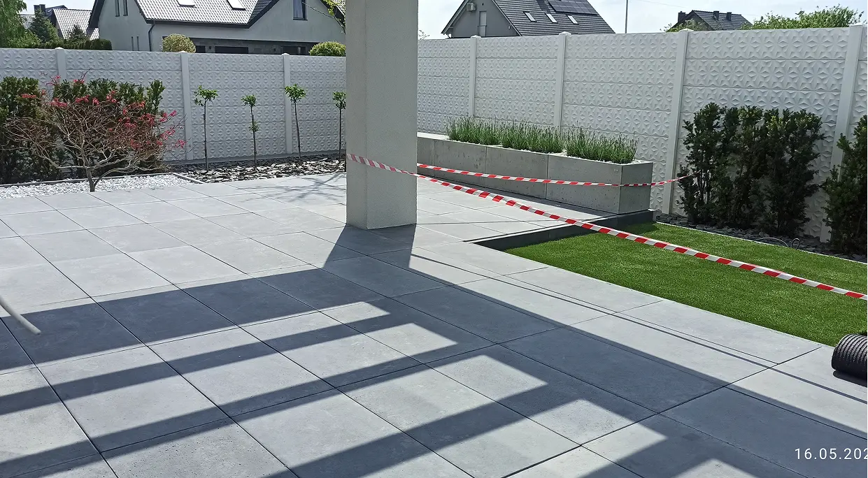 Płyty betonowe ułożone na tarasie z niwelacją terenu i pasem zieleni
